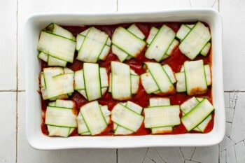 15 zucchini ravioli placed on top of sauce in a rectangular baking pan.