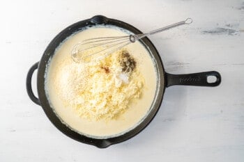 cheeses added to cheese sauce in a cast iron pan with a whisk.