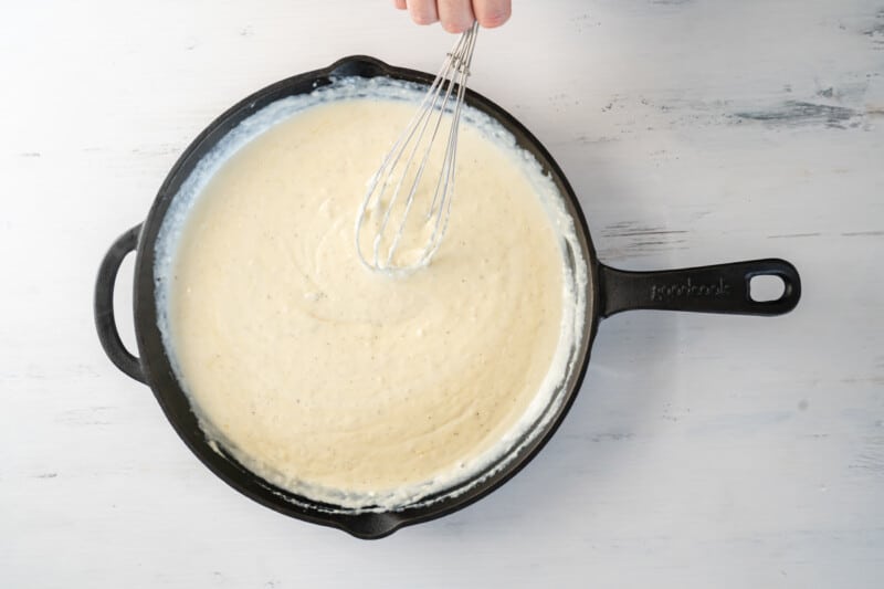 cheese sauce in a cast iron pan with a whisk.