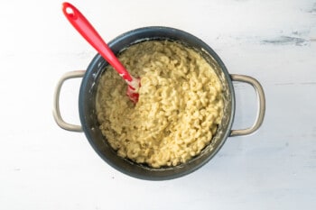 pesto mac and cheese in a large pasta pot with a red rubber spatula.
