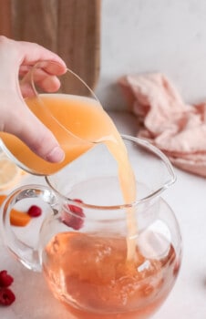 orange juice poured into a large glass pitcher filled with rose.