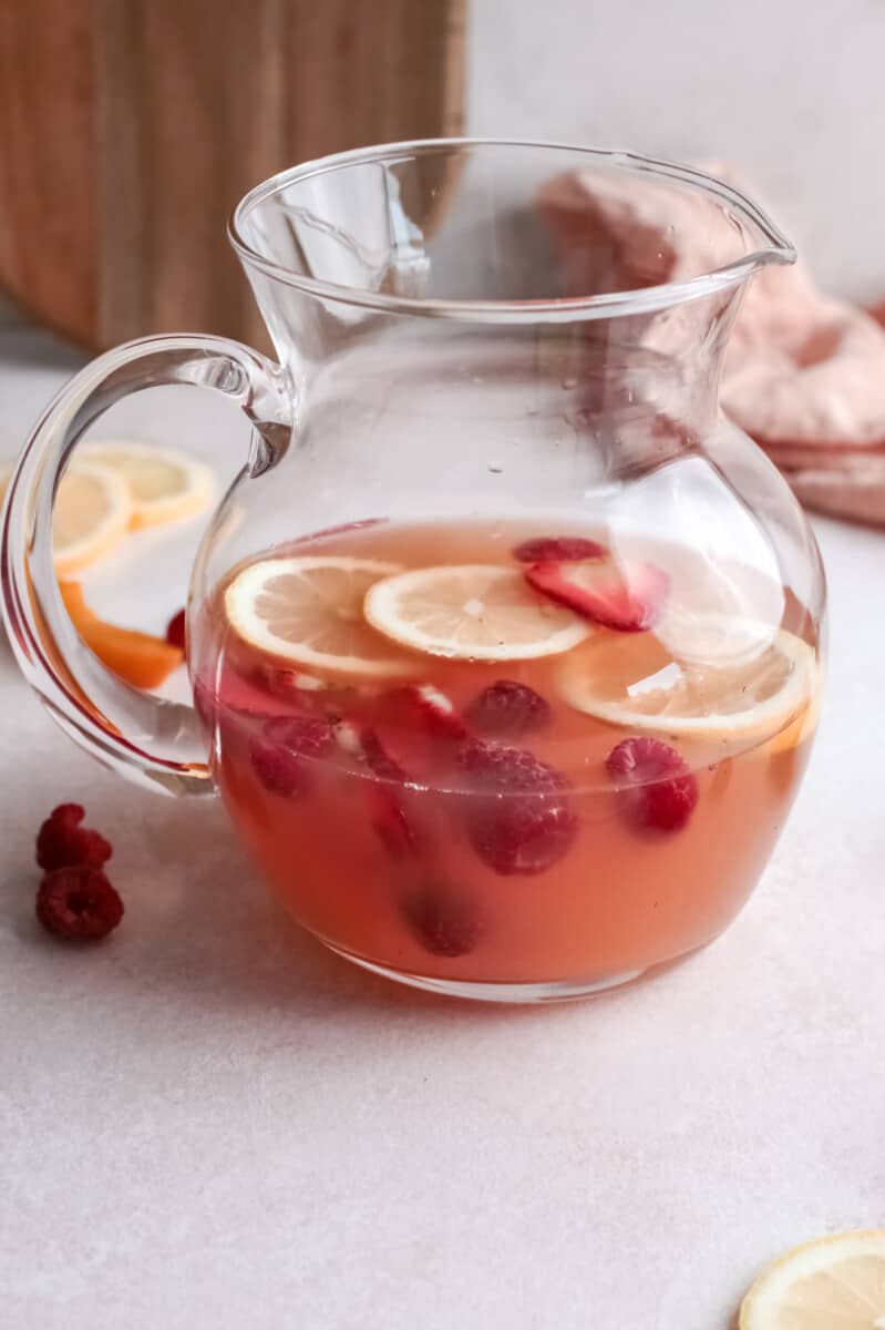 Rose sangria in a large glass pitcher with fruits.
