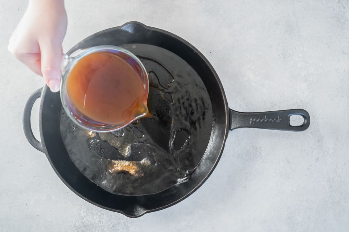 Beef broth added to a cast iron pan.