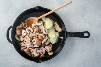 mushrooms and onions in a cast iron pan with a wooden spoon.