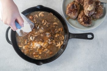 cornstarch mixture added to salisbury steak in a cast iron pan.