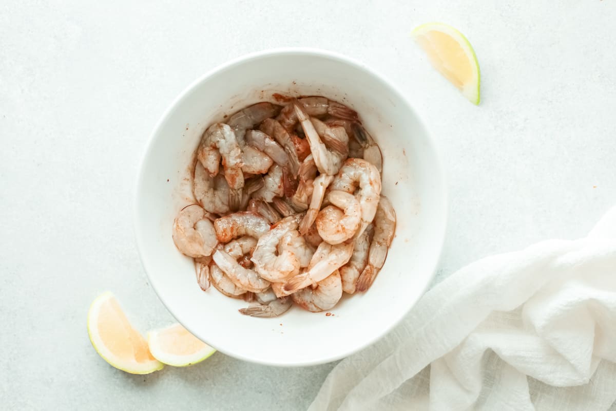 raw shrimp tossed in spices in a white bowl.