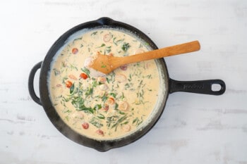tuscan salmon cream sauce in a cast iron pan with a wooden spoon.