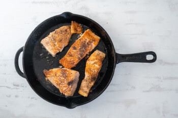 4 salmon filets cooking in a cast iron pan.