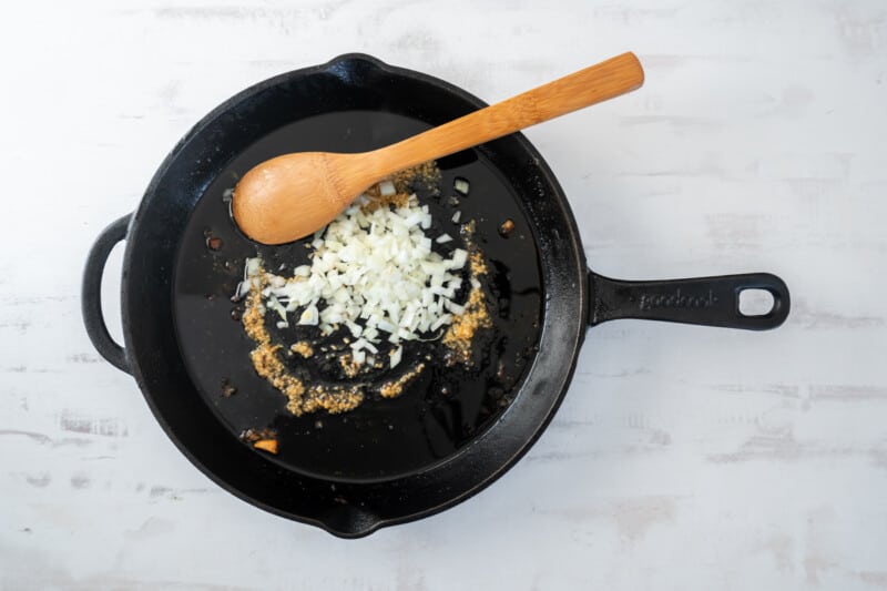 garlic and onion cooking in a cast iron pan with a wooden spoon.