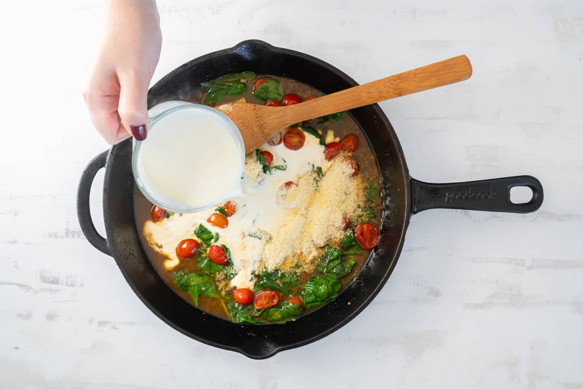 cream added to vegetables for tuscan salmon in a cast iron pan with a wooden spoon.