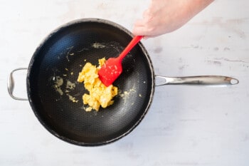 scrambled eggs in a wok with a red rubber spatula.