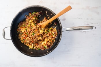 vegetable fried rice in a wok mixed together with a wooden spoon.