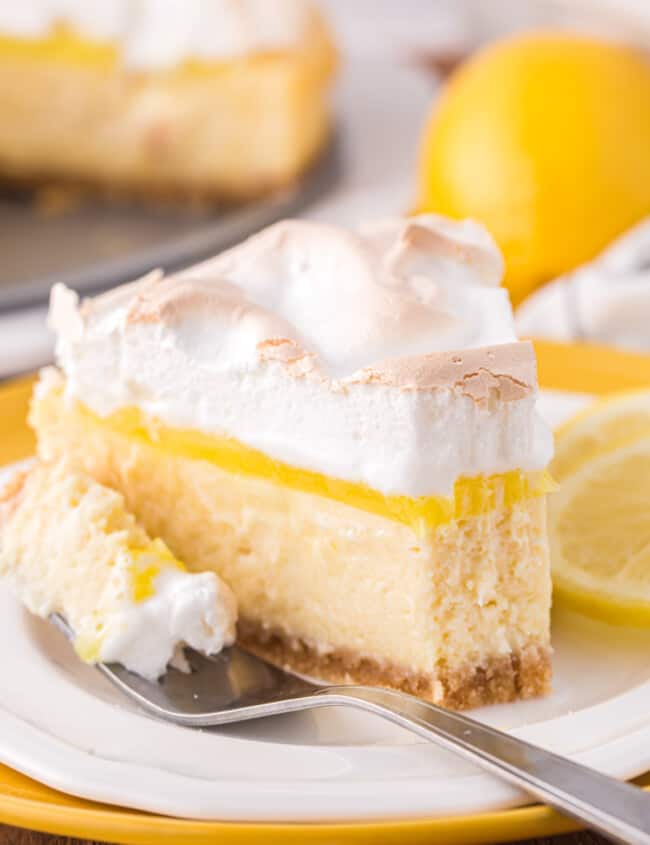 a partially eaten slice of lemon meringue cheesecake on a white plate with a fork.