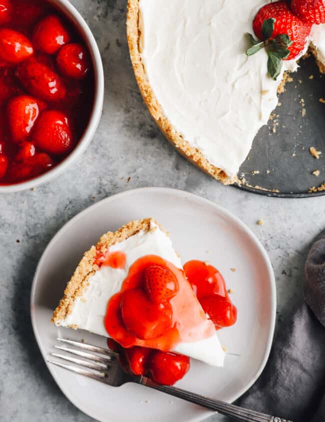 overhead view of a slice of no bake cheesecake on a white plate with strawberry topping and a fork.