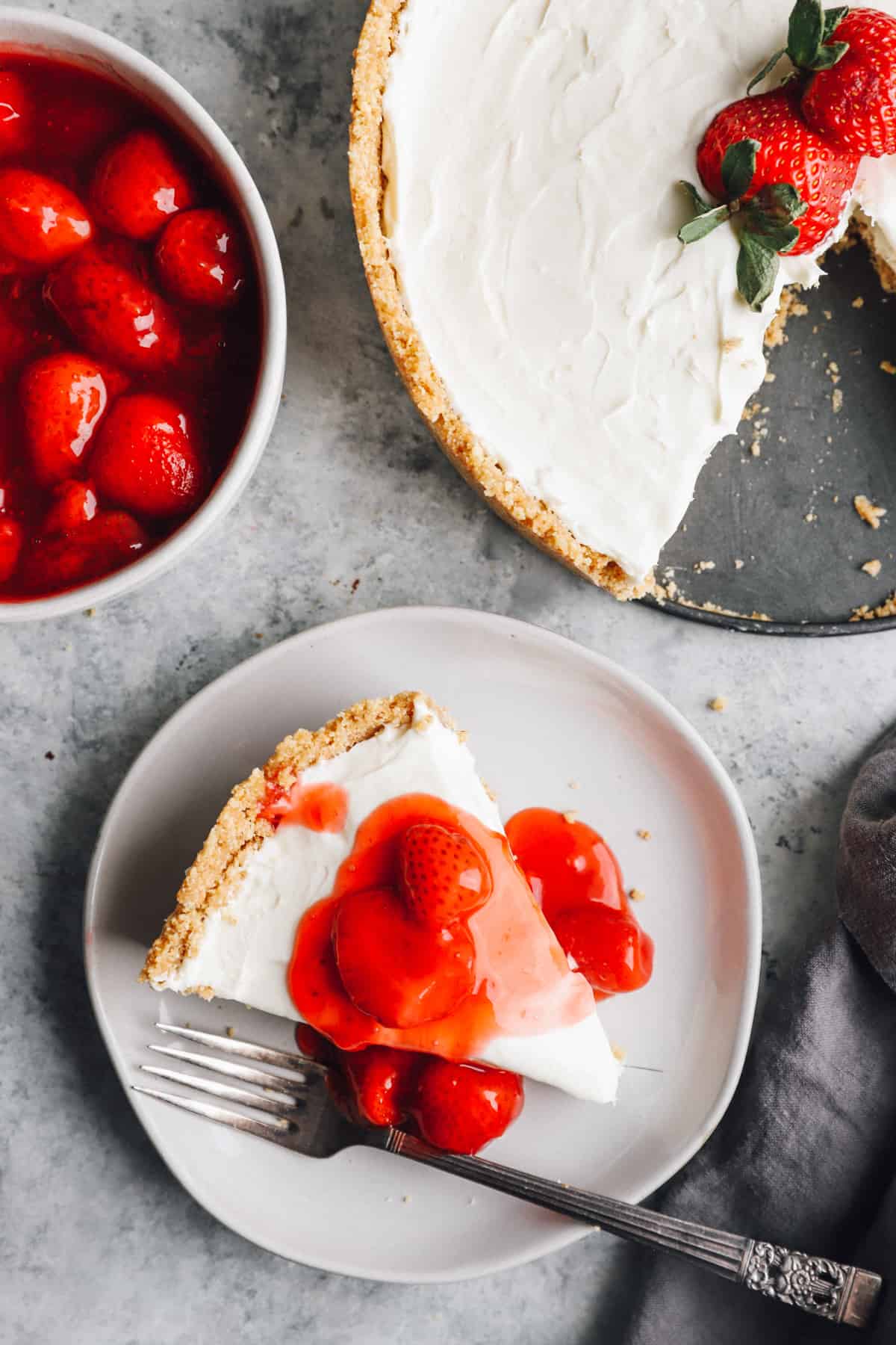 overhead view of a slice of no bake cheesecake on a white plate with strawberry topping and a fork.