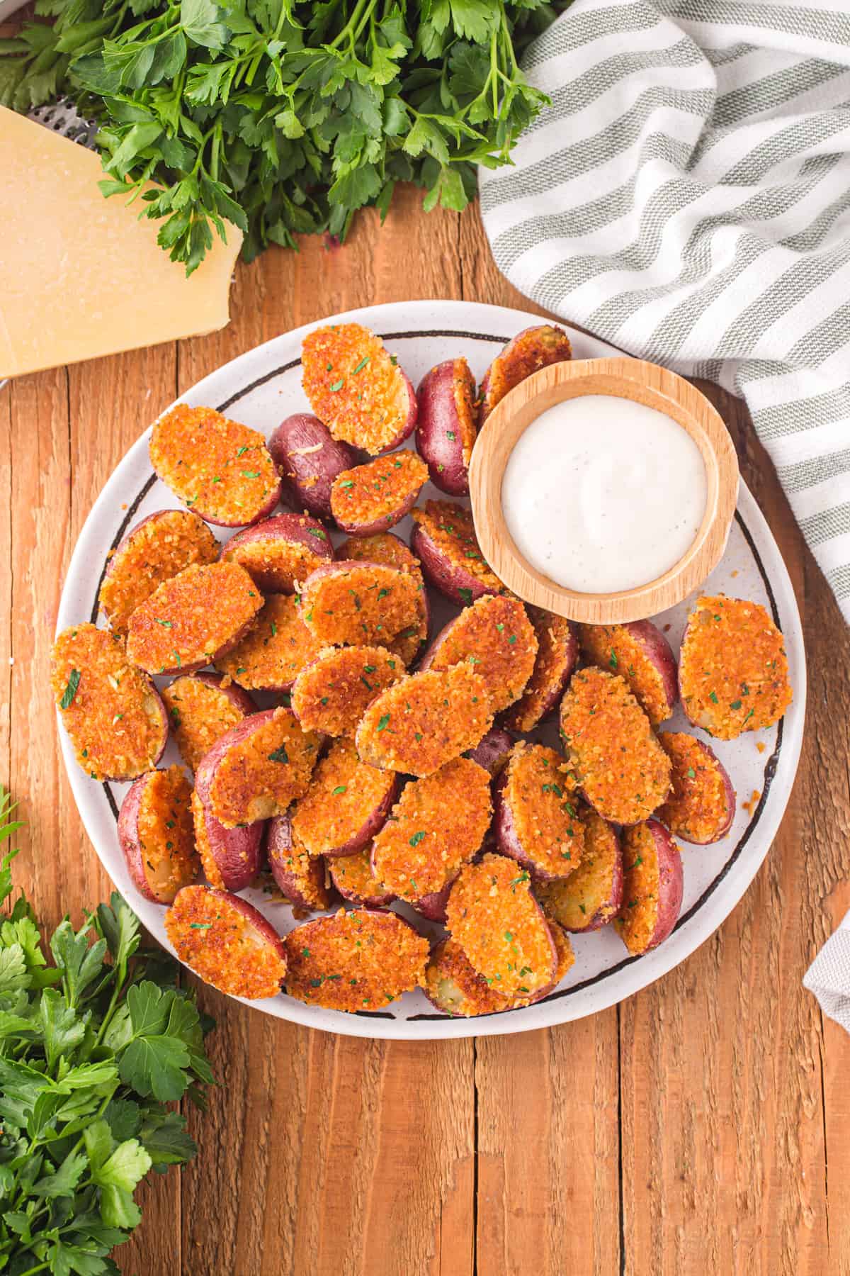 overhead view of roasted baby potatoes with parmesan breadcrumb crust, on a white serving platter with sour cream.