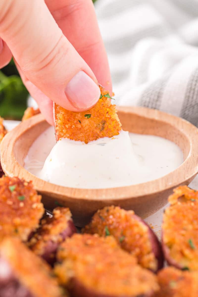a hand dipping a parmesan roasted potato into a dish of sour cream.
