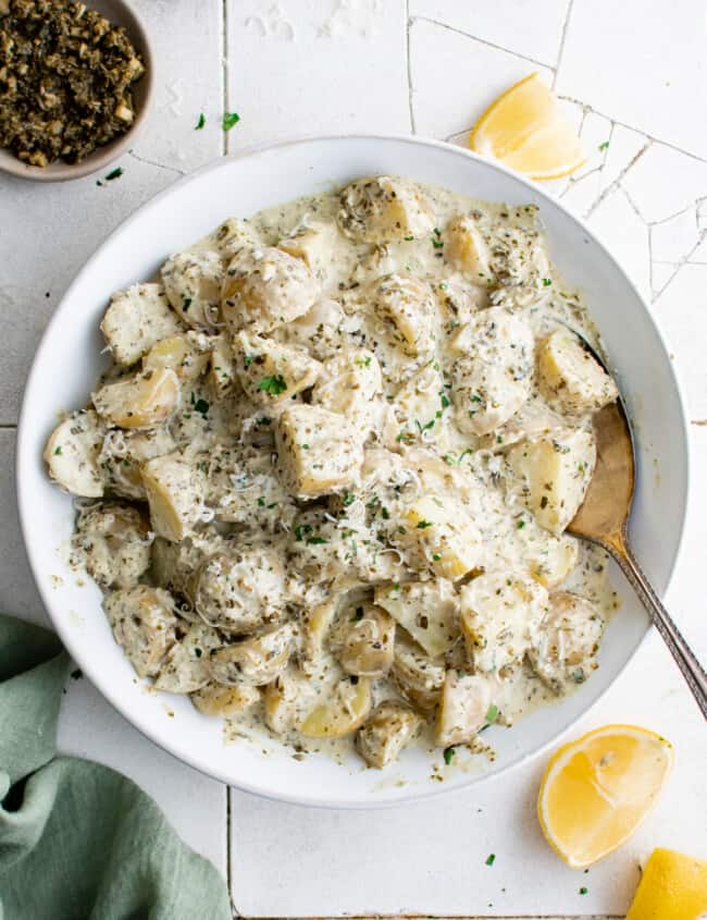 overhead view of pesto potato salad in a white bowl with a spoon.