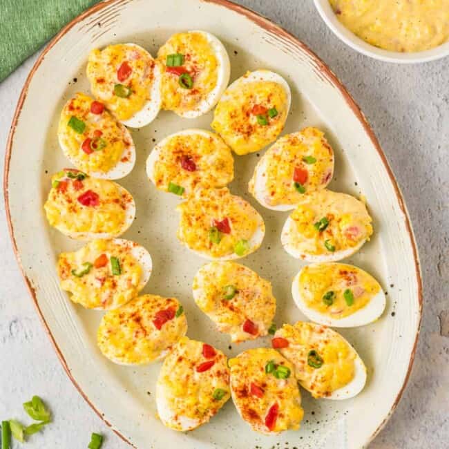 overhead view of pimento cheese deviled eggs on a white oval serving tray.