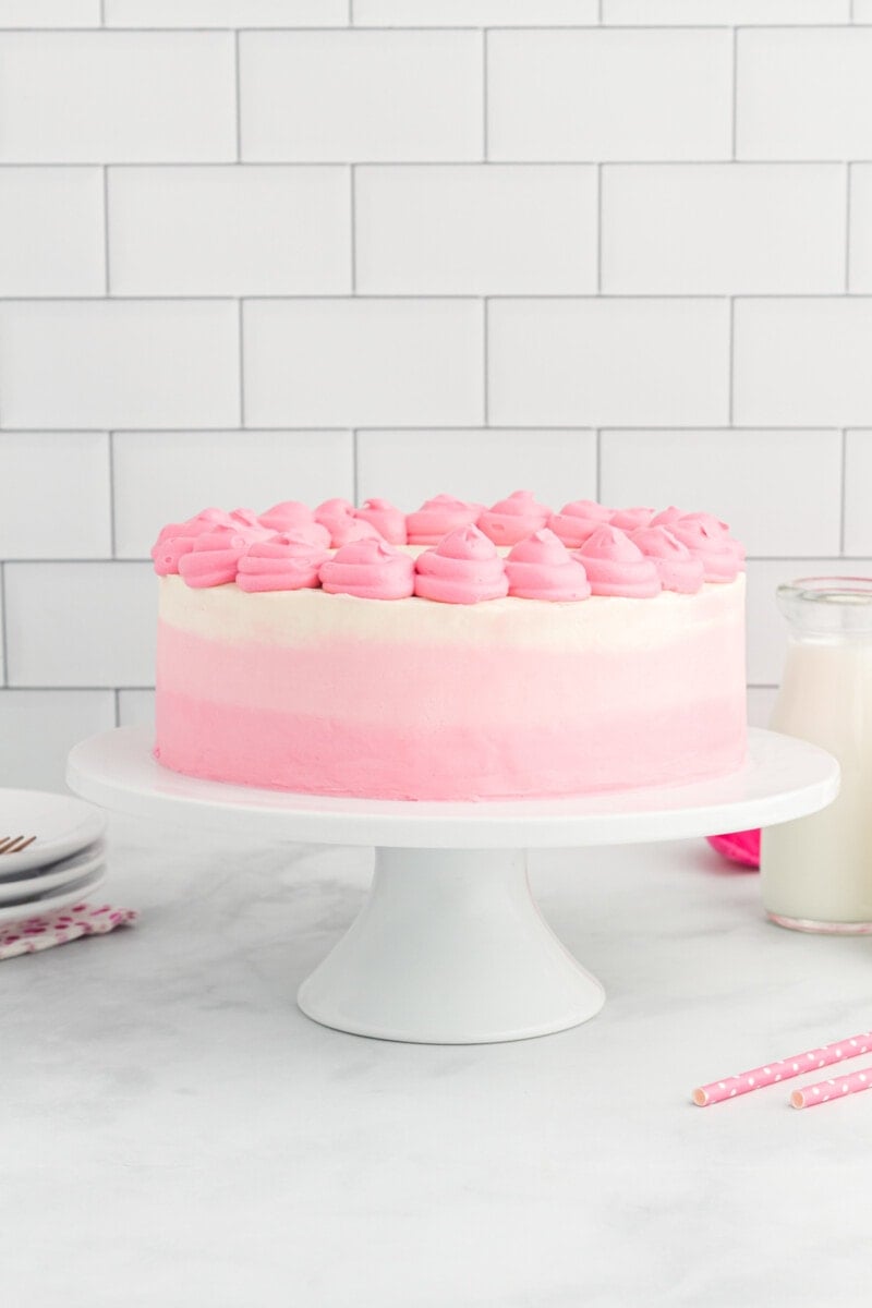 side view of ombre frosted pink velvet cake on a white cake stand with pink frosting swirls on top.