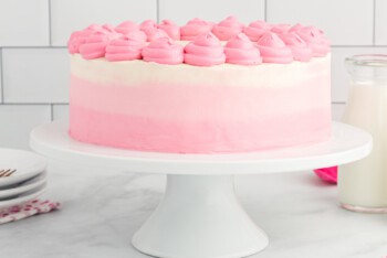 side view of ombre frosted pink velvet cake on a white cake stand with pink frosting swirls on top.