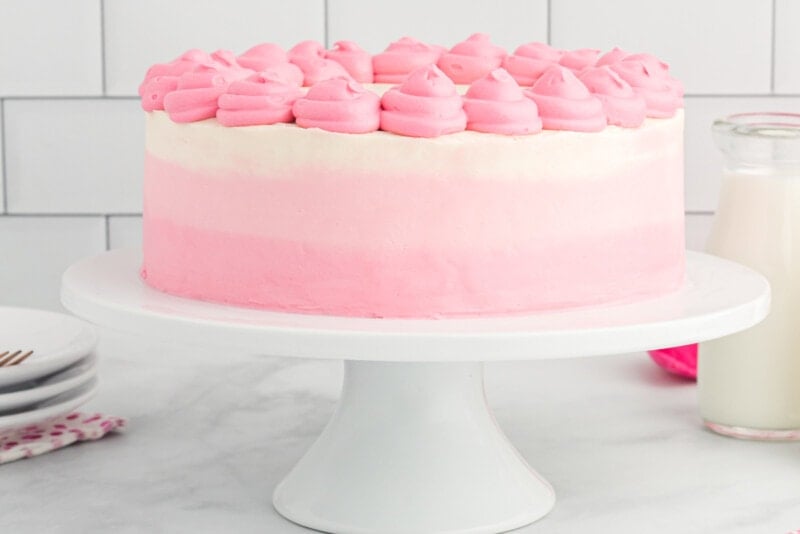 side view of ombre frosted pink velvet cake on a white cake stand with pink frosting swirls on top.