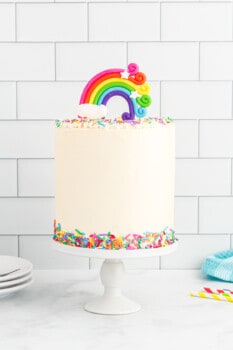 side view of rainbow cake on a white cake stand.