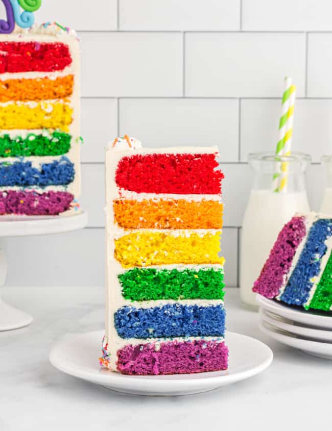 side view of a slice of rainbow cake on a white plate.