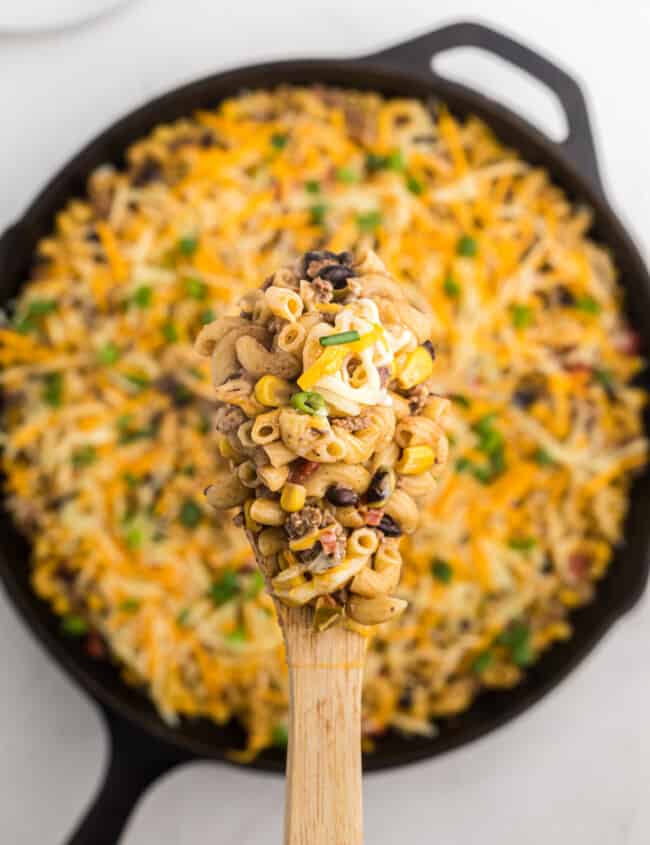 overhead view of taco mac and cheese in a cast iron pan with a wooden spoon.
