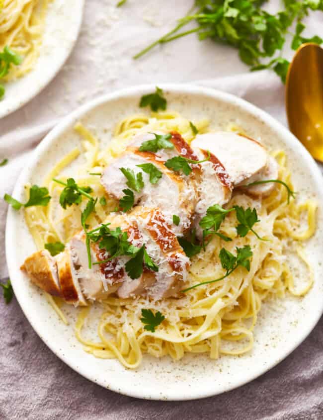 overhead view of a serving of chicken alfredo on a white plate.