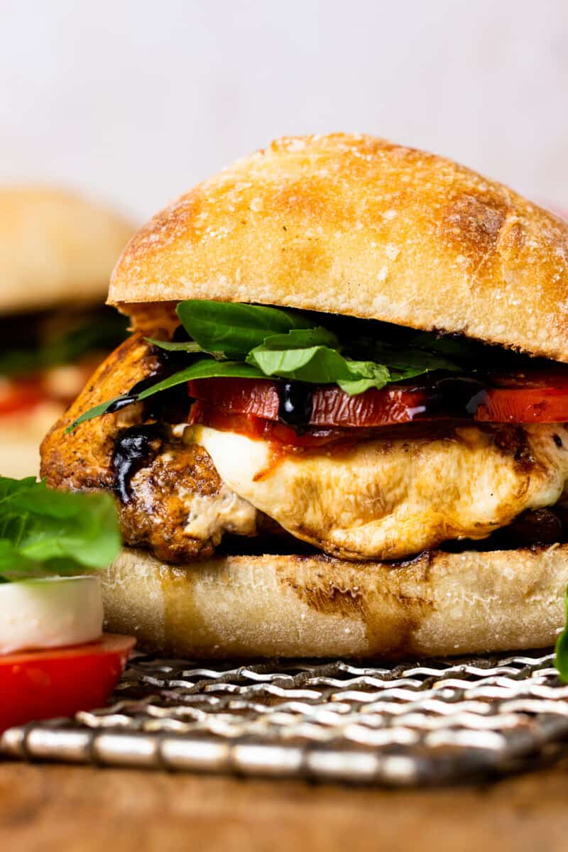 close up side view of a chicken caprese sandwich on a wicker placemat.