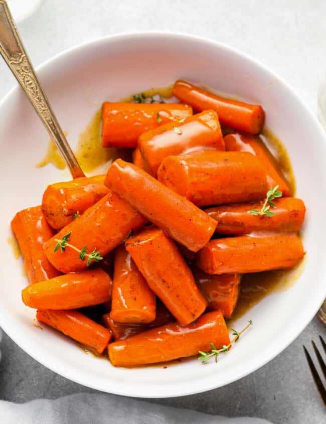 crockpot carrots in a white bowl with a serving spoon.