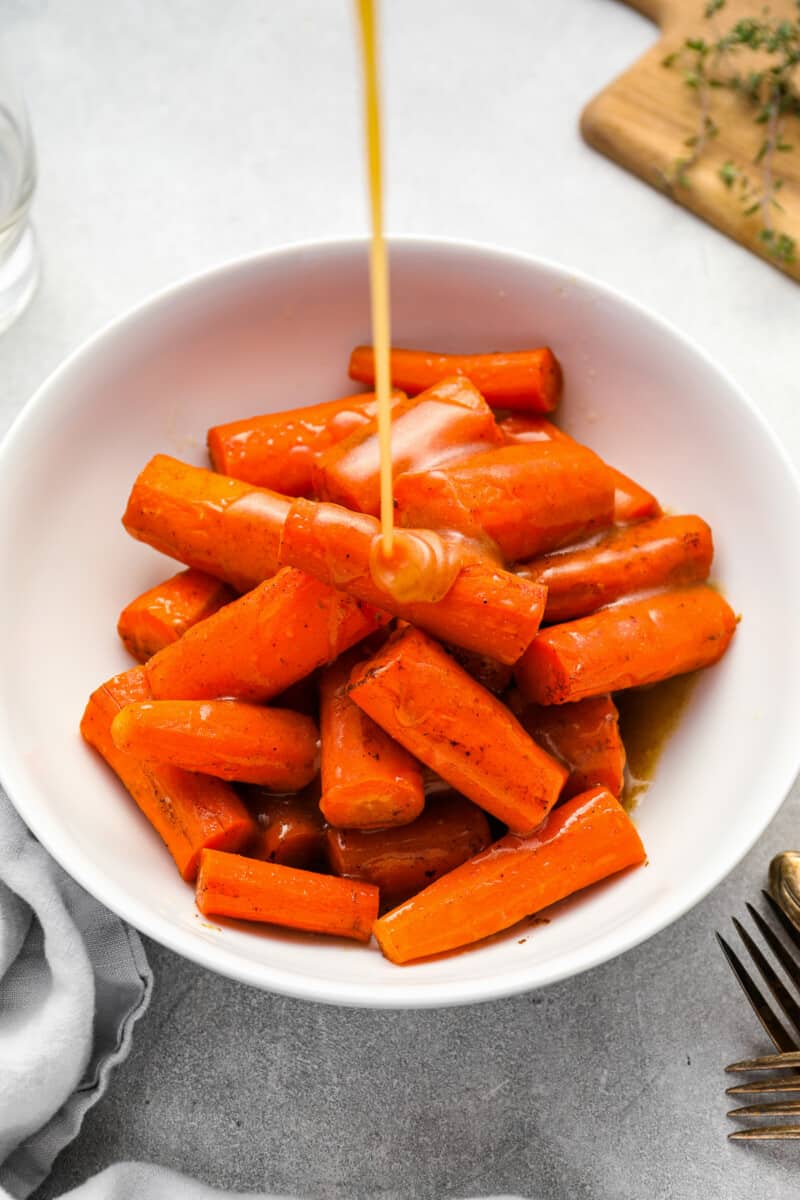 glaze poured over crockpot glazed carrots in a white bowl.