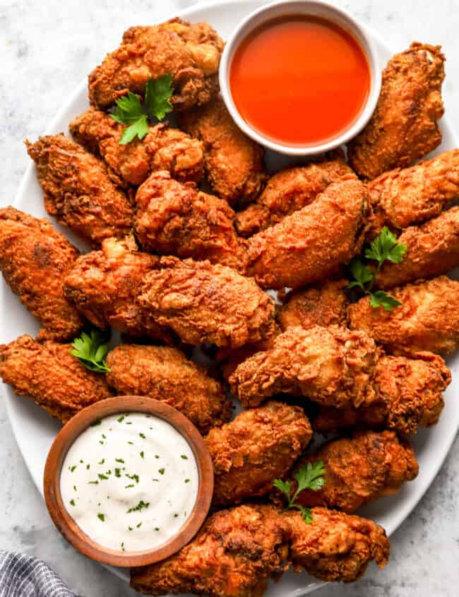 overhead view of fried chicken wings on a white platter with buffalo sauce and ranch.