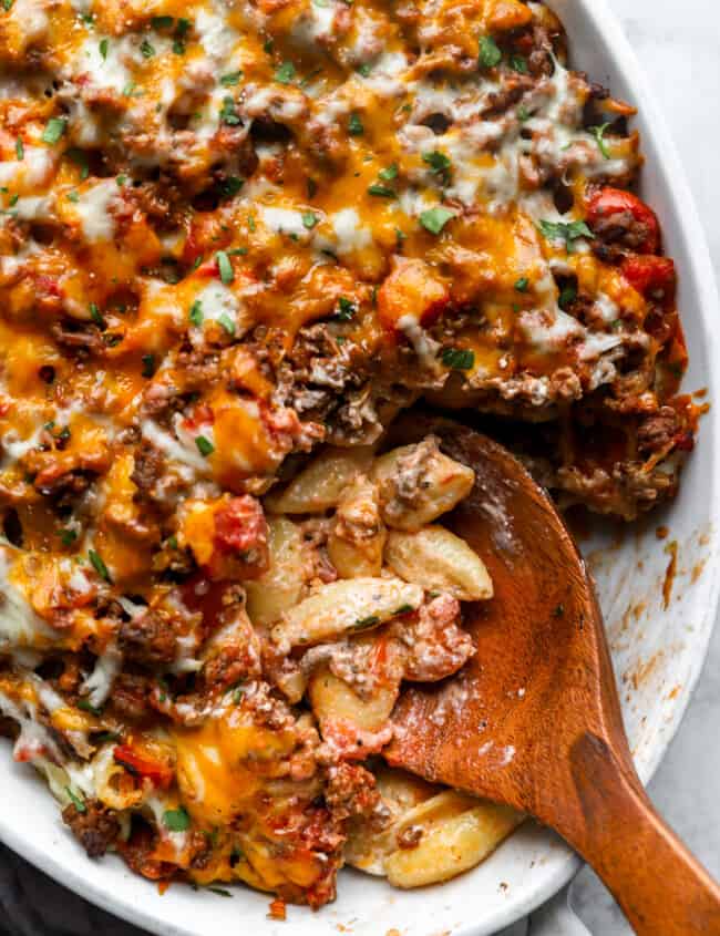 overhead view of hamburger casserole in a white oval casserole dish with a wooden spoon.