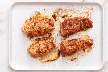 overhead view of 4 seasoned chicken thighs on a baking sheet.