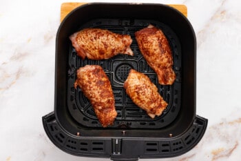 overhead view of 4 seasoned chicken thighs in an air fryer basket.