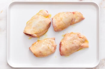 overhead view of 4 raw chicken thighs on a baking sheet.