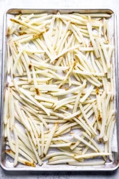 raw french fries spread out on a baking sheet.