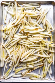 raw french fries on a baking sheet drizzled with olive oil.