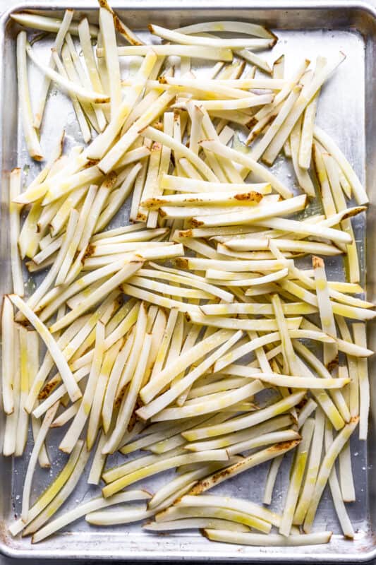 raw french fries on a baking sheet drizzled with olive oil.