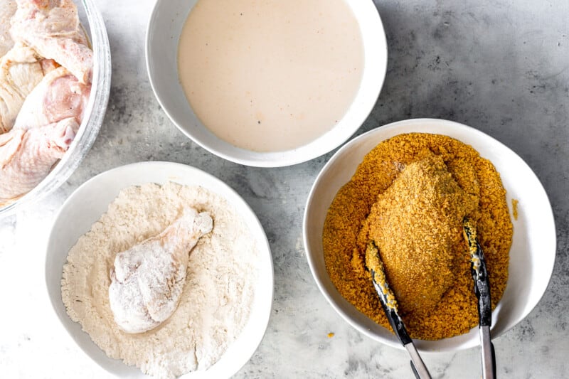 overhead view of chicken pieces being dredged through milk, flour, and breadcrumbs.