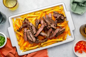 strips of steak on top of cheesy french fries on a white tray.