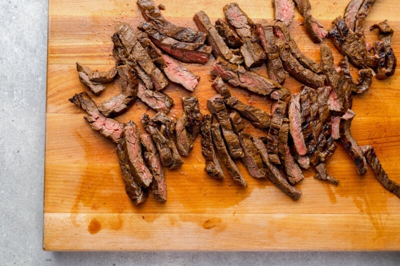 sliced cooked skirt steak on a wooden cutting board.