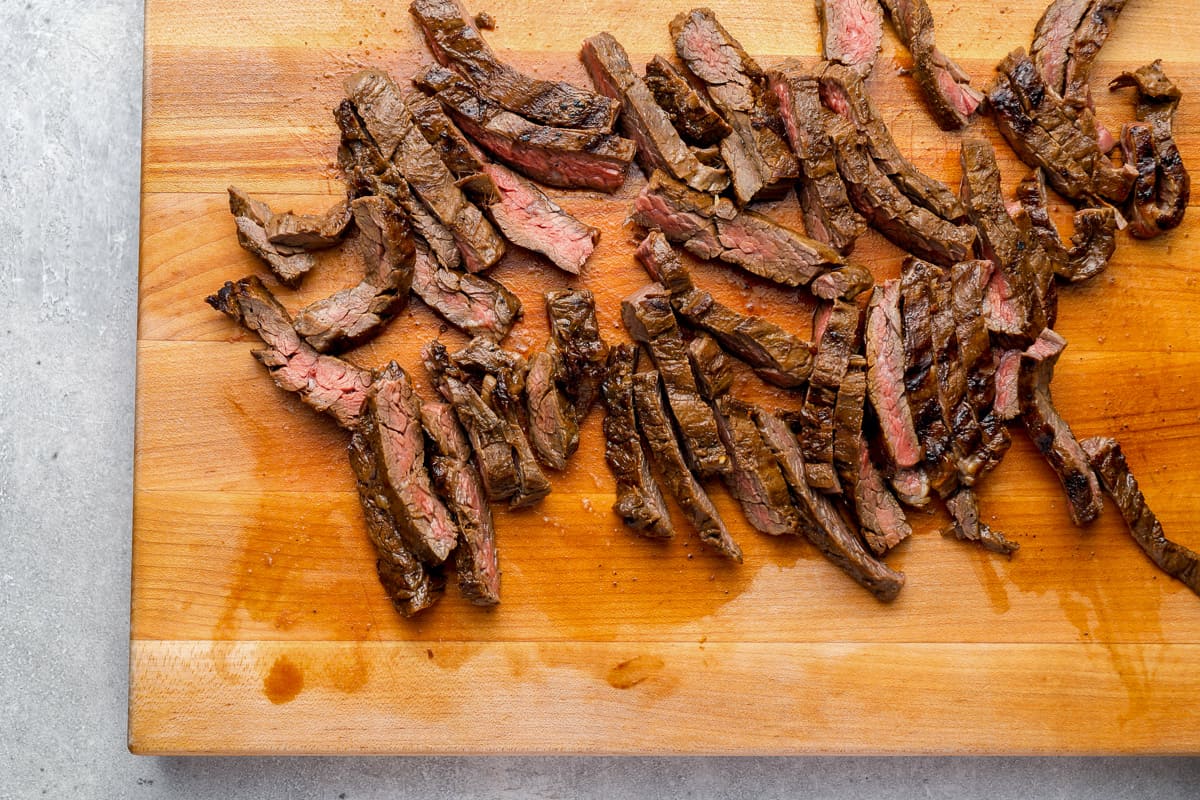 Sliced cooked skirt steak on a wooden cutting board.