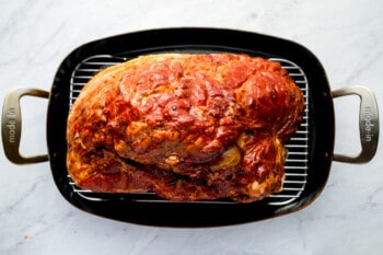 a roasted turkey in a roasting pan on a marble countertop.