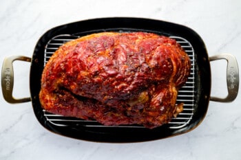 a roasted ham in a pan on a marble countertop.