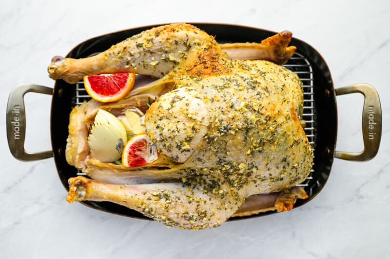 a roasted turkey in a pan on a marble countertop.