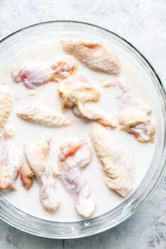 overhead view of chicken wings marinating in buttermilk in a glass bowl.