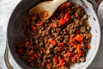 beef and peppers cooking in a frying pan with a wooden spoon.